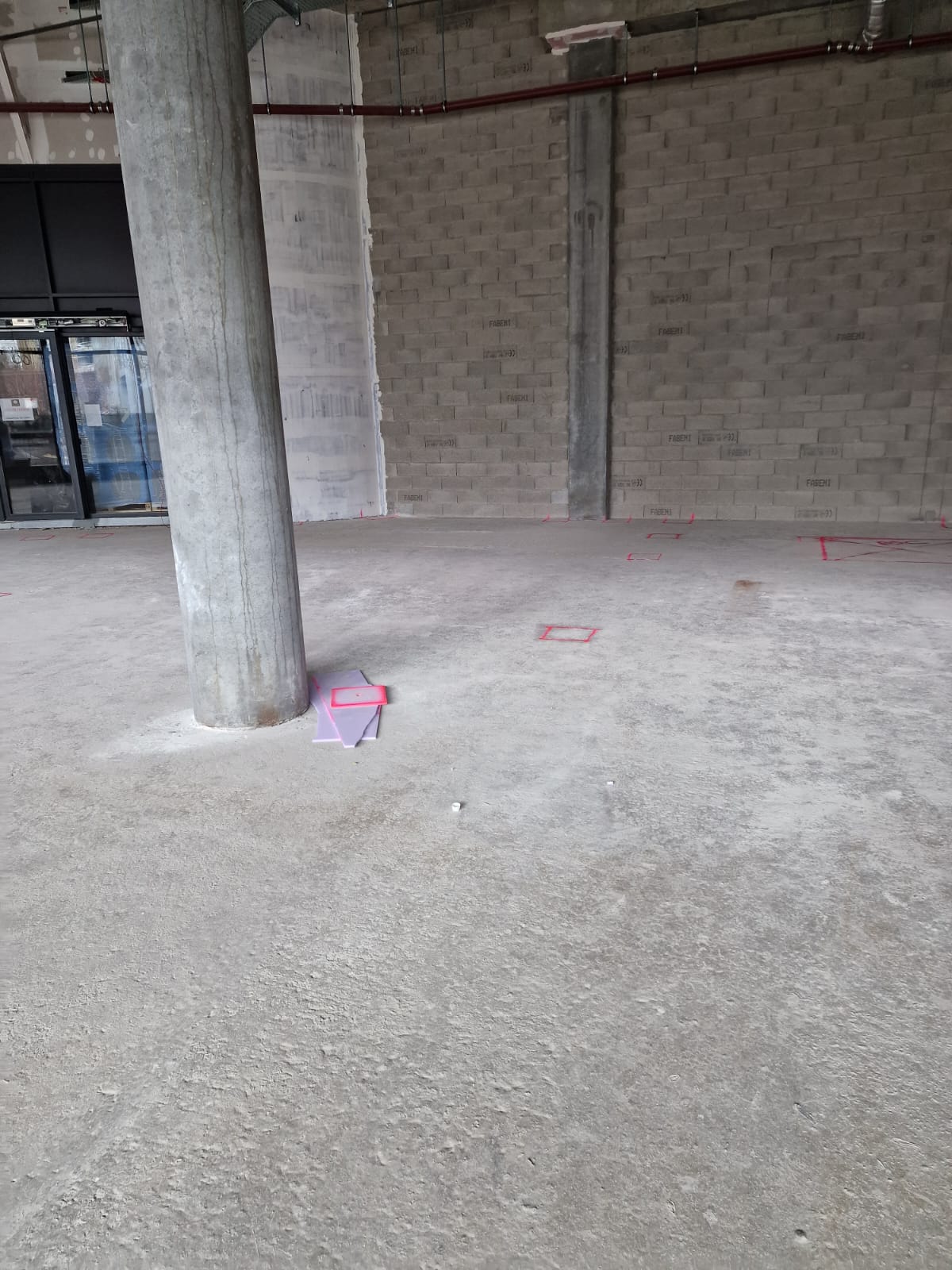 Intérieur brut avec colonne en béton, murs en maçonnerie et marquages roses au sol
