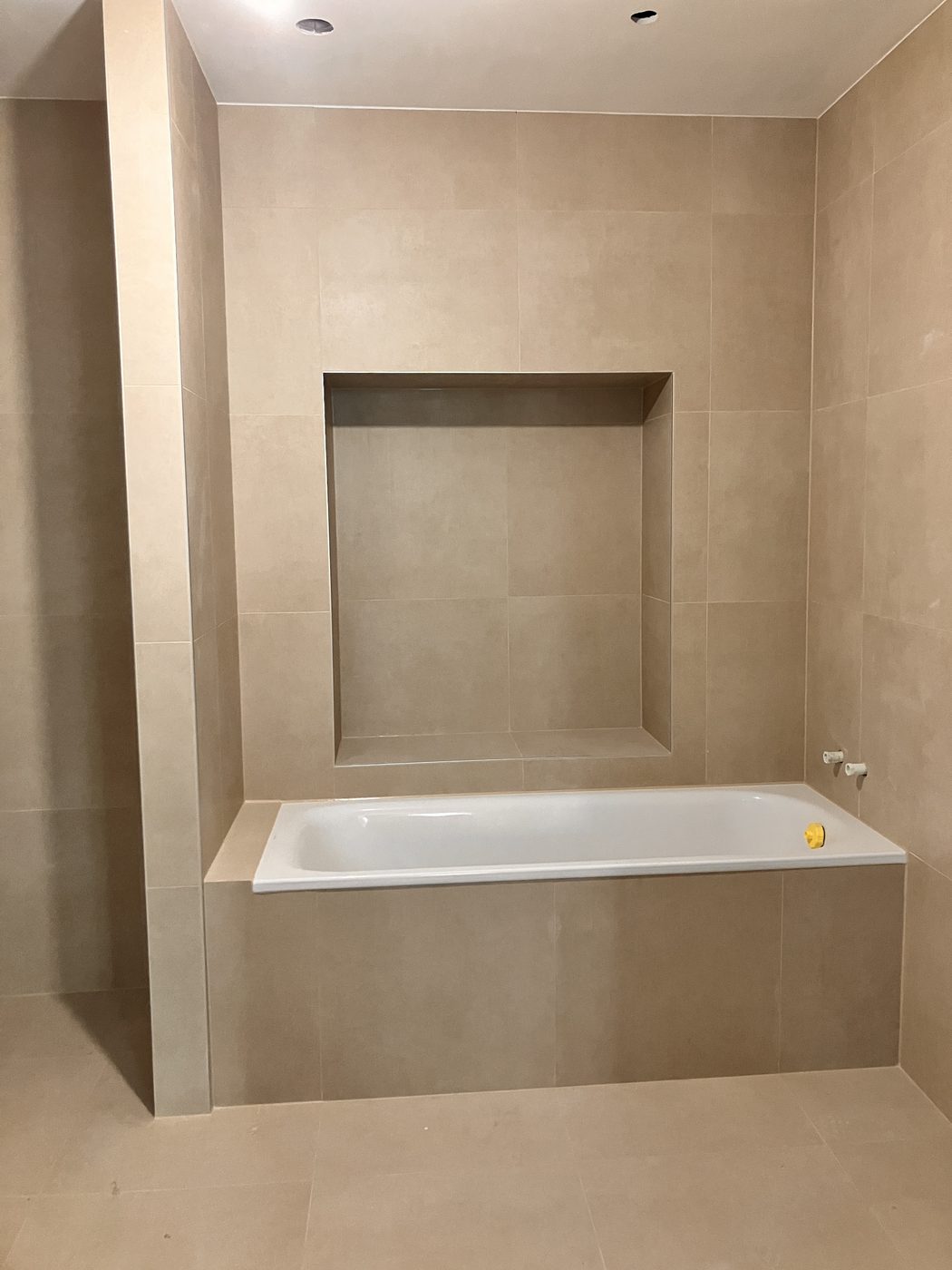 Salle de bains carrelée en grandes dalles beiges avec baignoire et niche, à Genève